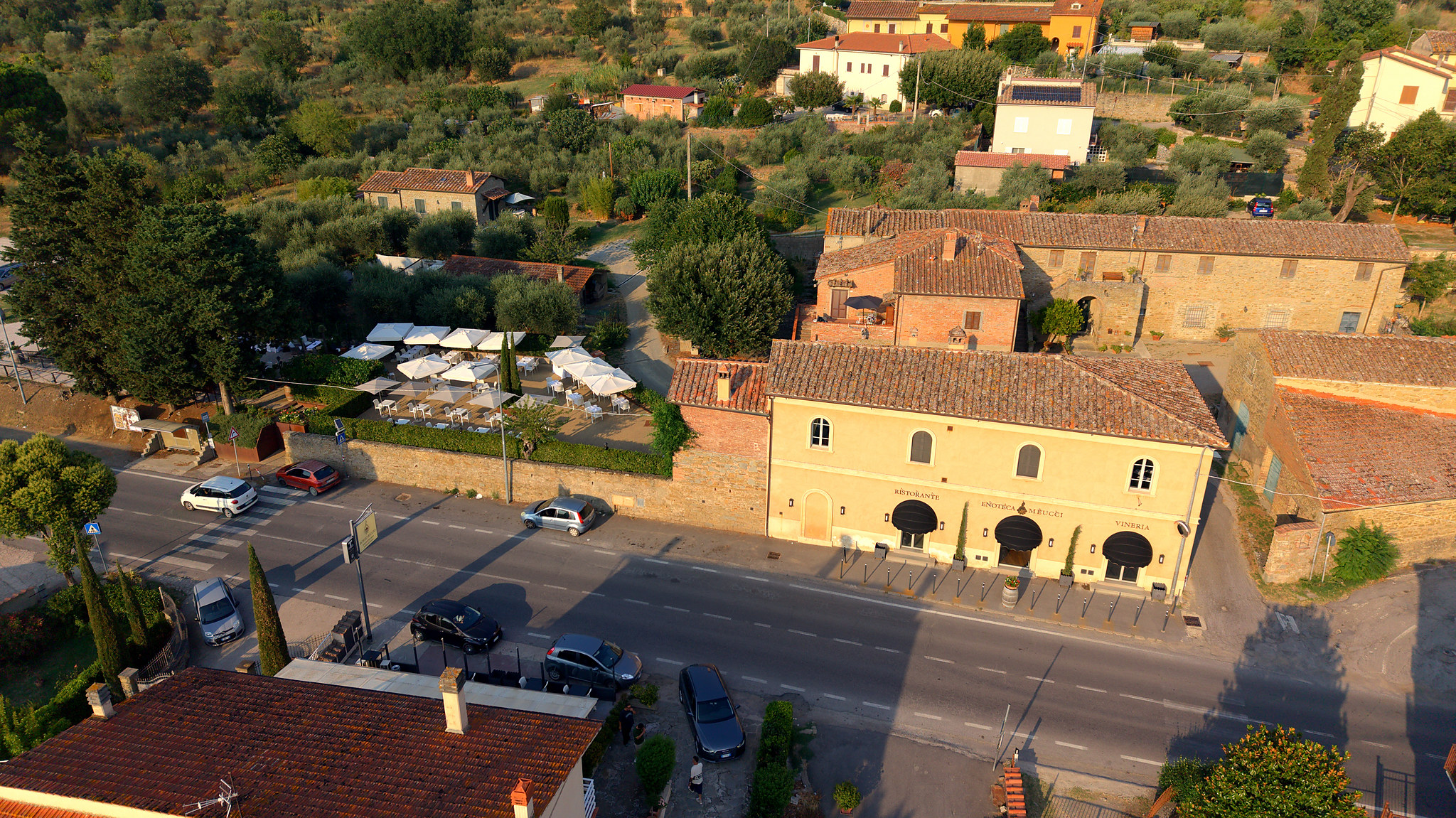 Vista aerea del casale dell'Enoteca Meucci: il dehors con gli ombrelloni e le tre arcate sulla strada.