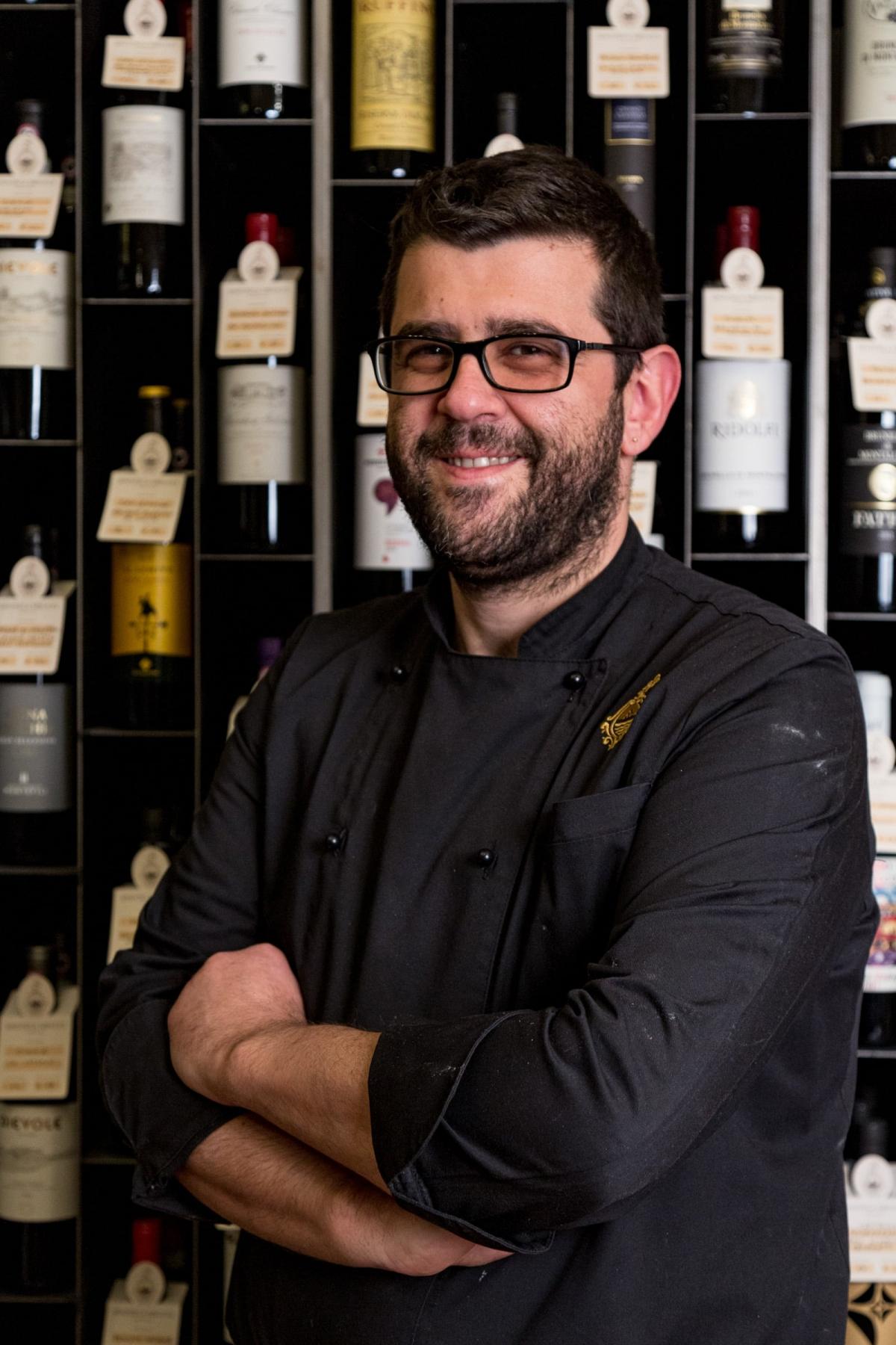Lo chef Massimo Romano davanti alla parete delle bottiglie