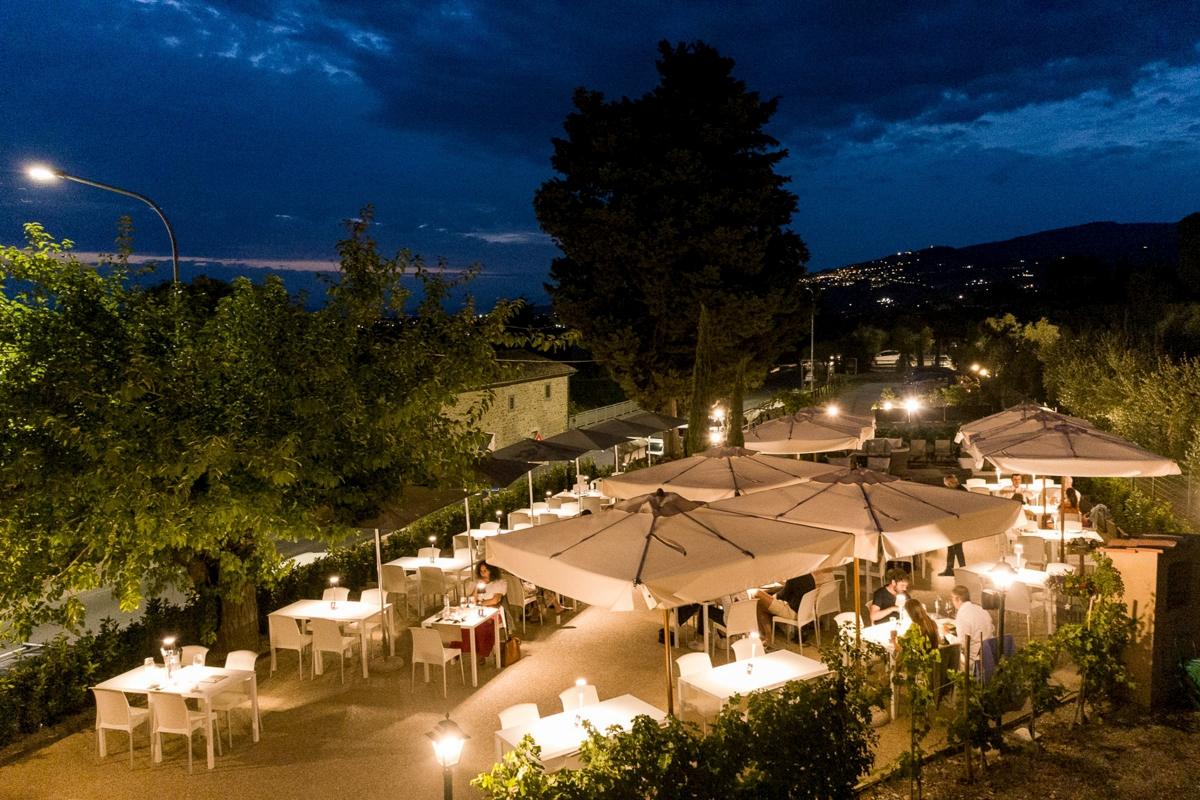 Il giardino al crepuscolo visto dall’alto: gli ombrelloni bianchi accesi dalle lanterne e il cipresso contro il cielo blu