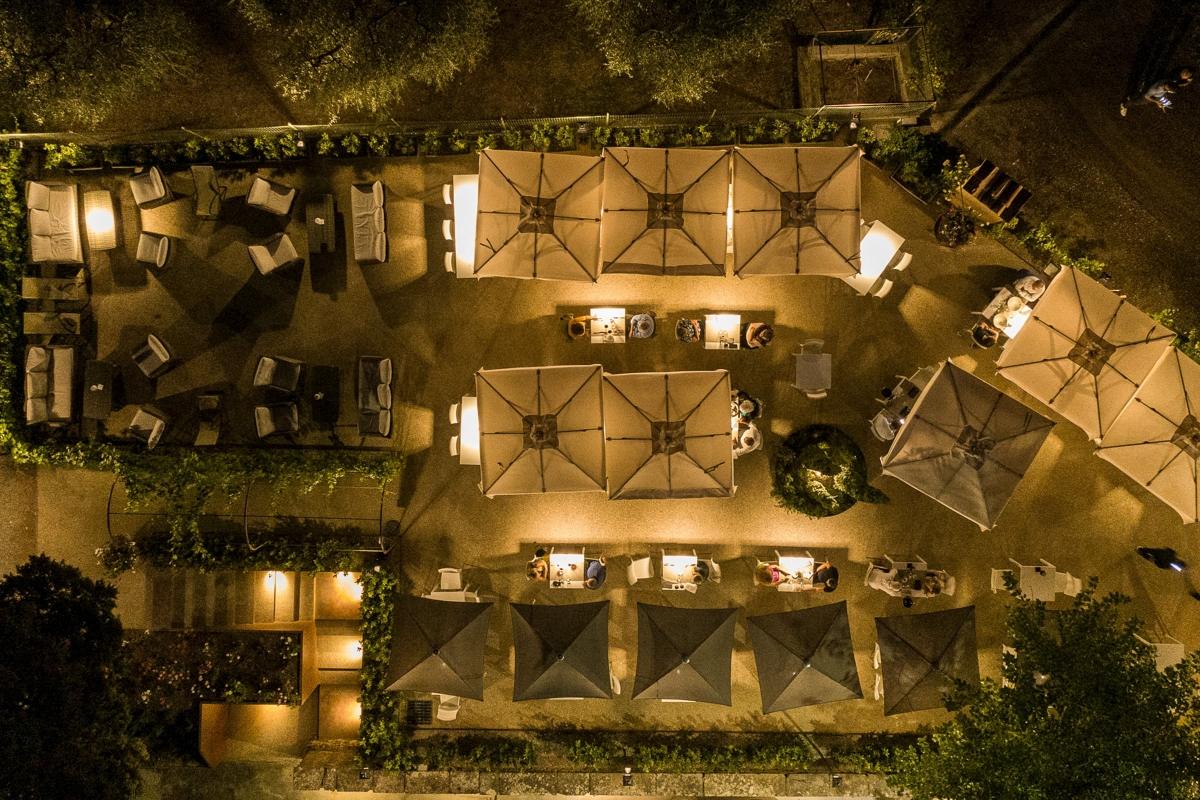 La ripresa verticale dal drone: le file di ombrelloni chiari e scuri, i tavoli accesi e i divani sulla ghiaia