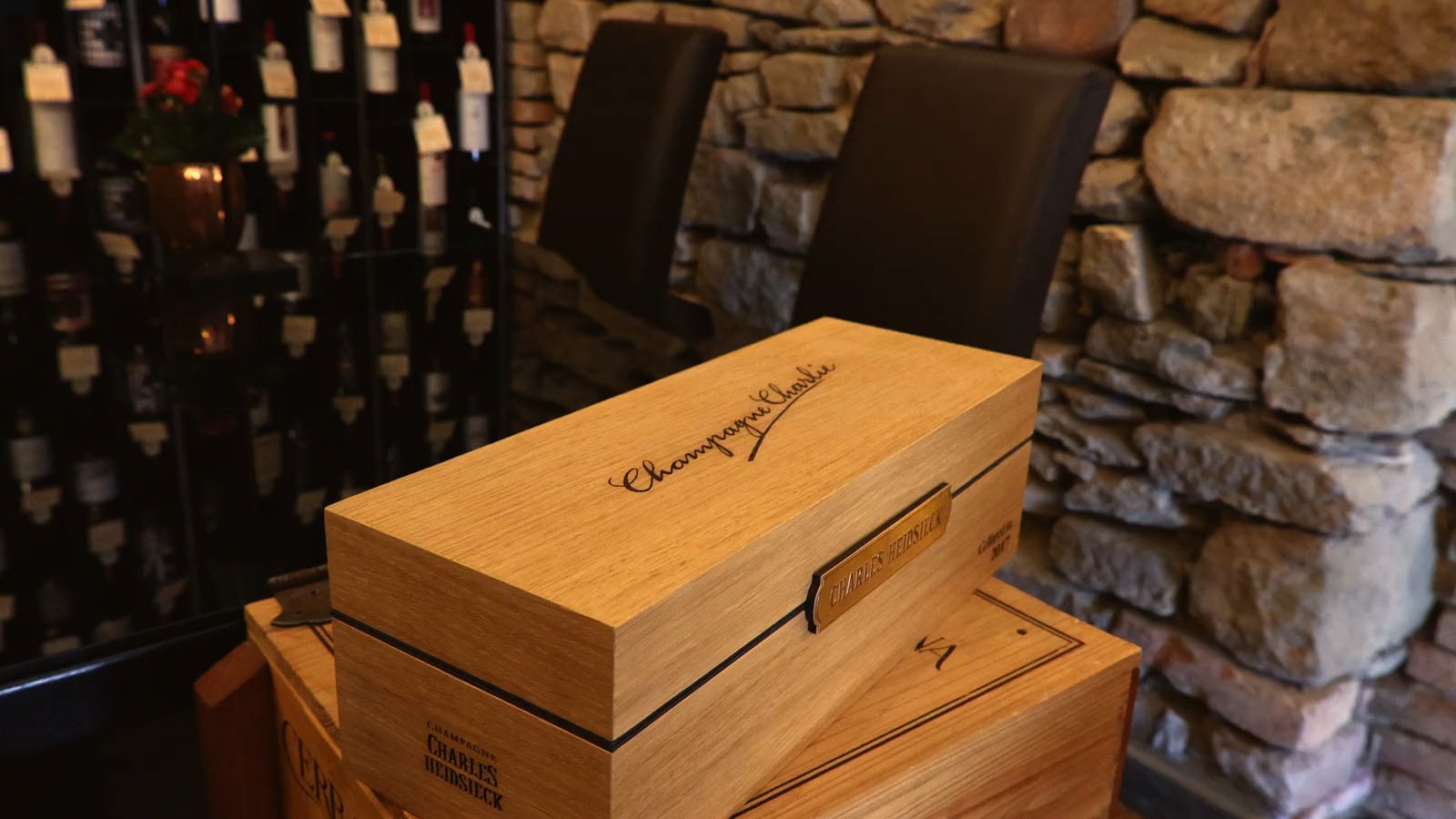 Due mani aprono la cassa di legno di uno Champagne, davanti alla parete di bottiglie